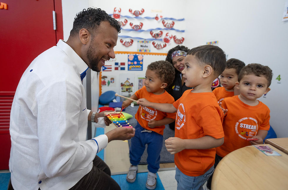 Niños de edad preescolar tocan un xilófono que sostiene el director ejecutivo de la Red durante una actividad musical en un salón de clases.