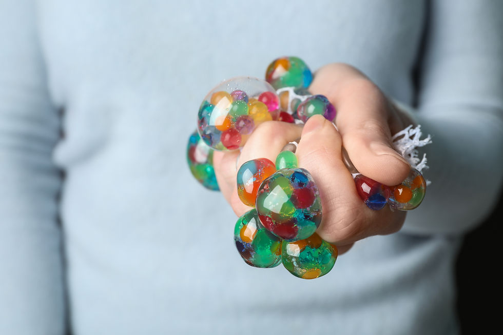 Primer plano de una mano que aprieta una pelota sensorial transparente con bolitas de colores en su interior.