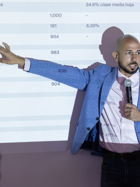 El Dr. José Caraballo Cueto señala datos estadísticos proyectados durante la presentación del estudio Movilidad Social en Puerto Rico, celebrada en la Fundación Luis Muñoz Marín el 12 de mayo de 2026. La pantalla muestra una tabla con distribución por clase social y grupos de edad.