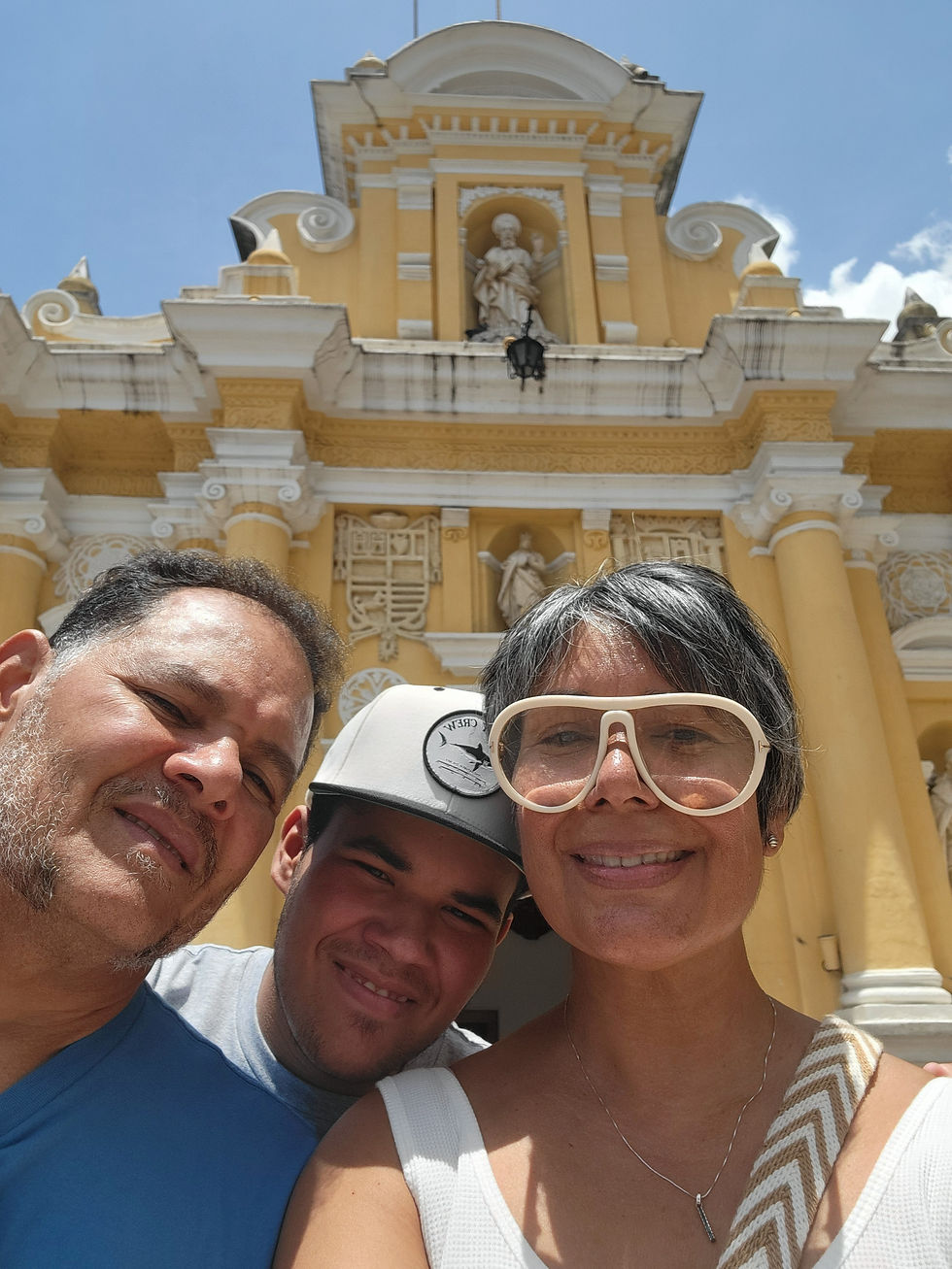 José, Franco y Militza posan para una fotografía familiar frente a la fachada amarilla y blanca de una iglesia.