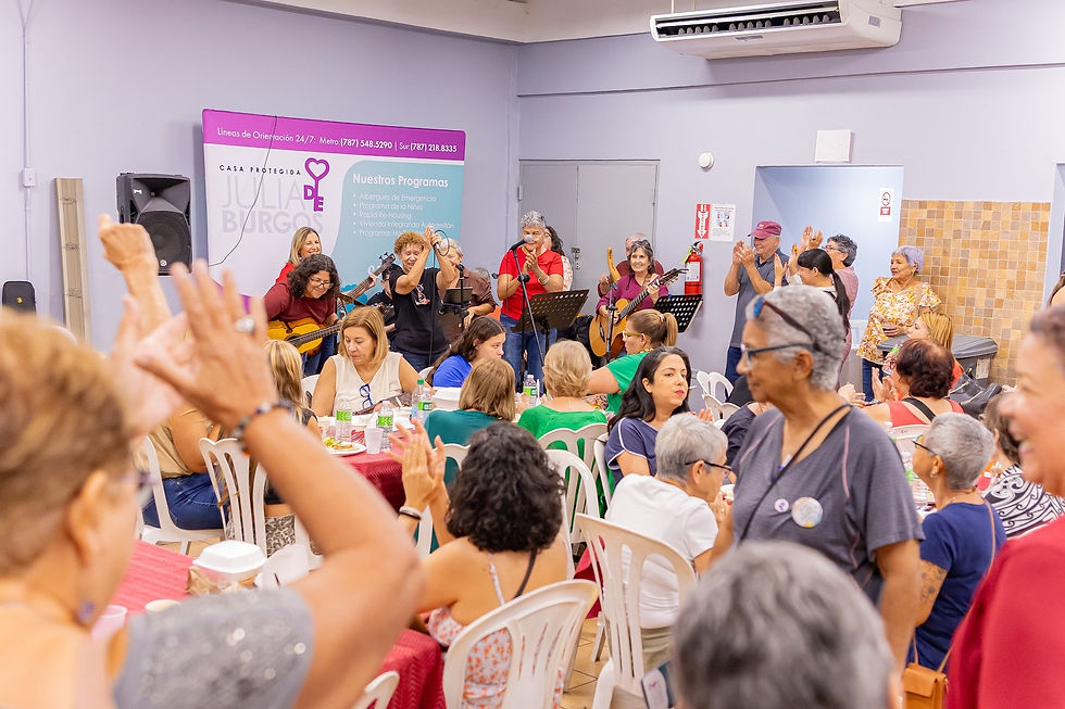 Participantes aplauden mientras un grupo toca guitarras y canta durante una actividad de Casa Protegida Julia de Burgos.