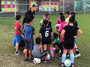 Entrenador del Oratorio San Juan Bosco rodeado de niños y jóvenes durante una práctica de fútbol en el parque comunitario de Cantera, San Juan.