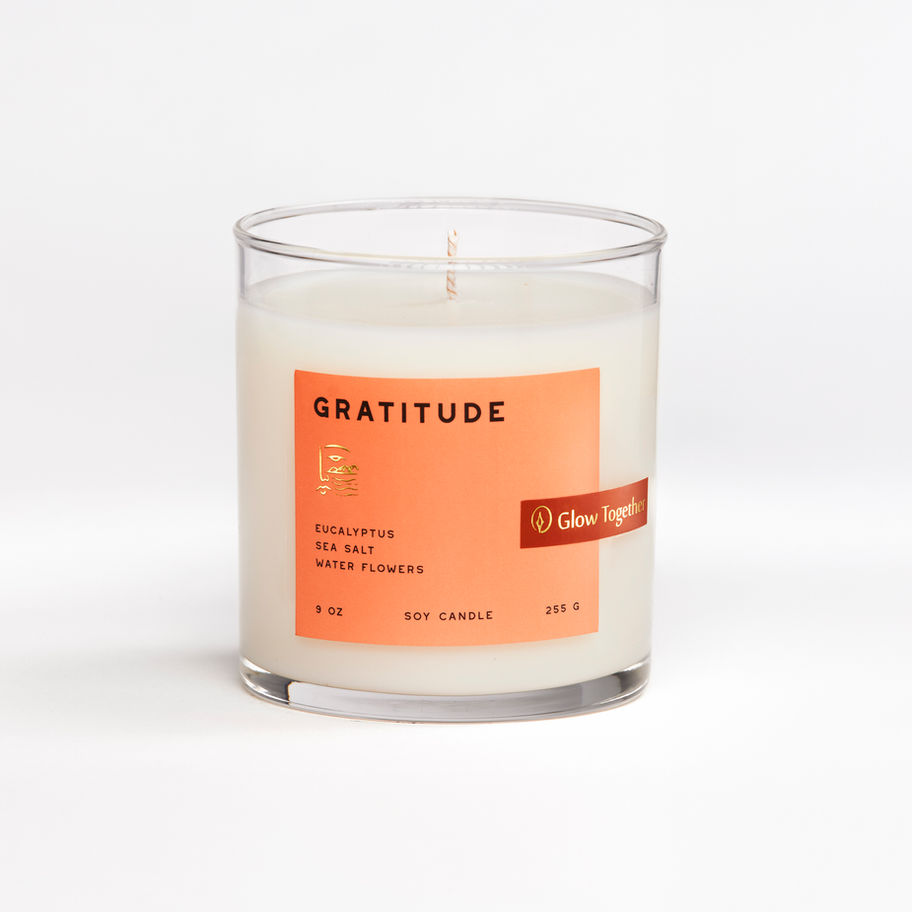 Glow Together Gratitude candle in clear glass with warm orange label, eucalyptus sea salt and water flowers scent