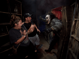 Two guests screaming as a monster lunges from a hidden panel during a live jump scare at The Nightmare Factory in Indiana