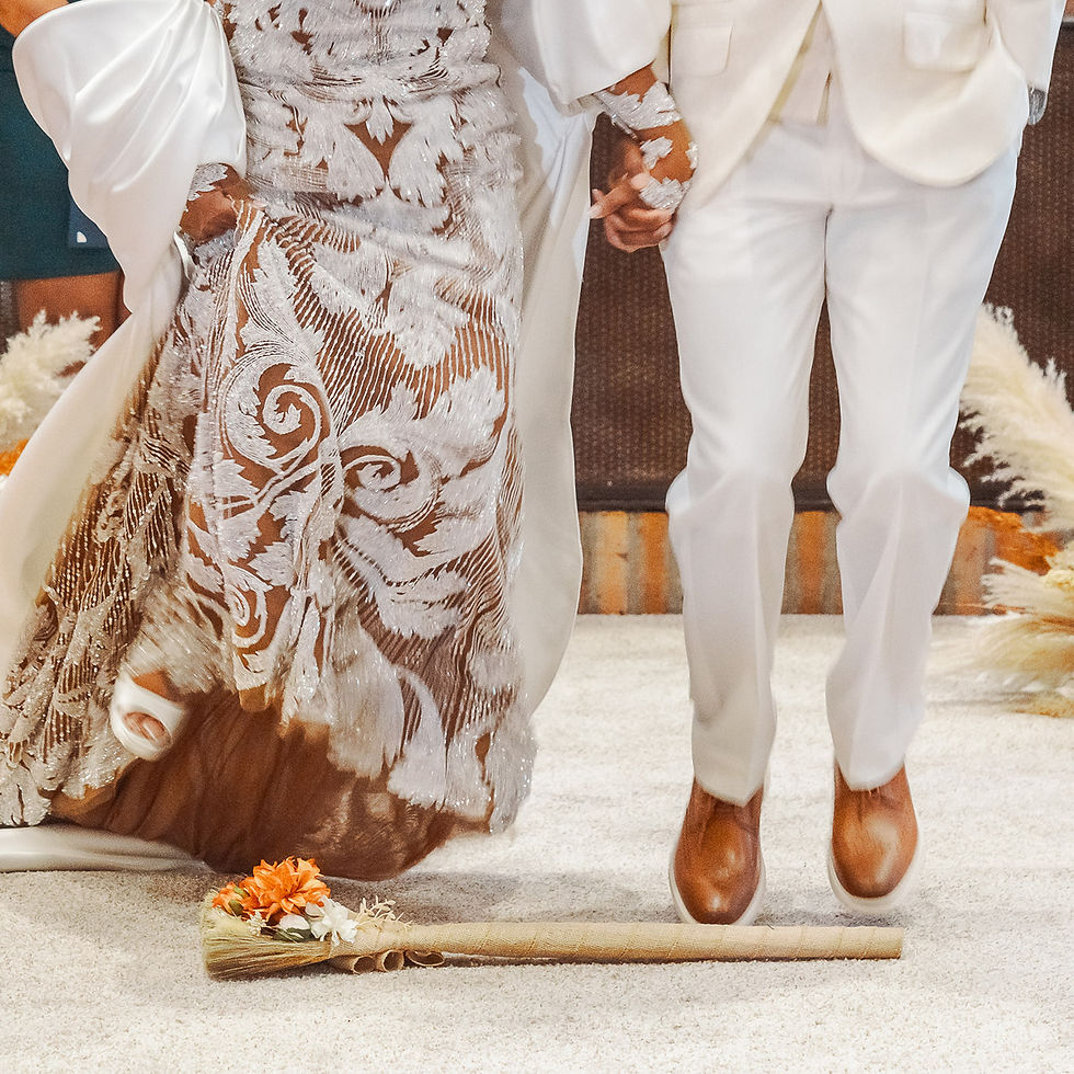 Bride in white lace gown and groom in white suit hold hands at an indoor wedding; bouquet rests on the carpet.