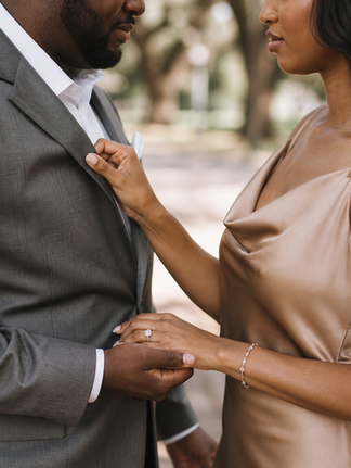 Close-up engagement photo of a Black couple holding hands while adjusting a suit jacket during a romantic City Park portrait session.
