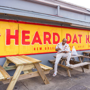 Man eating at picnic table outside Heard Dat Kitchen in New Orleans. Bright yellow and red mural background with casual atmosphere.
