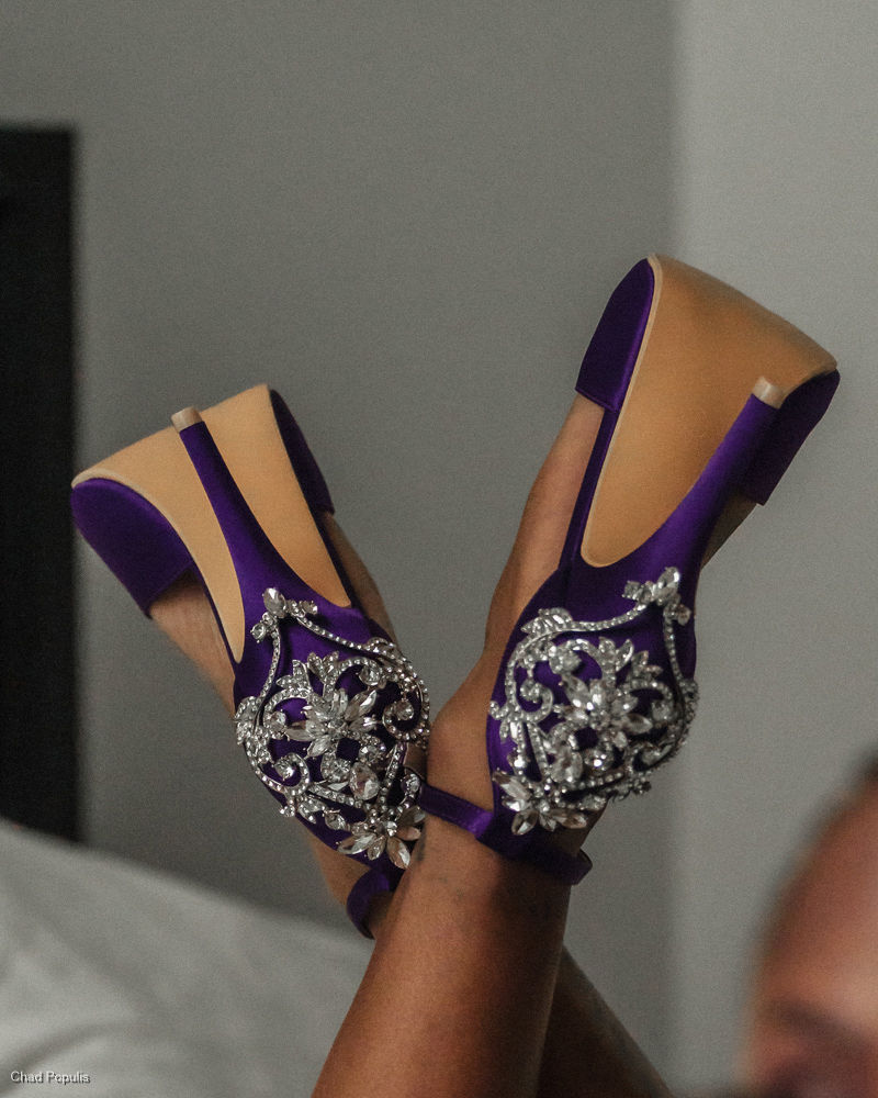 Crossed legs wearing purple-and-tan jeweled high-heeled shoes against a gray background, with a small Chad Papulis watermark.