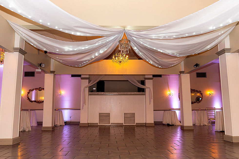Empty elegant banquet hall with white draped ceiling, chandeliers, purple uplights, and tiled floor, softly lit and formal