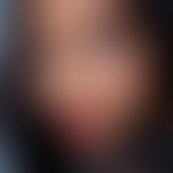 Close-up of a woman with bold red lipstick and colorful eye makeup, gazing confidently. Smooth skin, black hair, and sheer black attire.