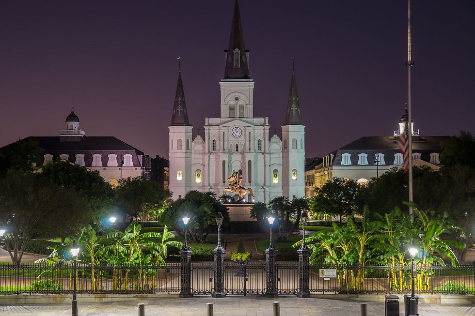 Illuminated cathedral with three spires at night, foreground statue, trees, and iron fence. Purple sky enhances the serene atmosphere.