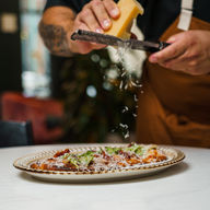 chef shaving parmesan over margarita flatbread pizza