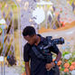 Young man holding a camera gimbal, looking down. Elegant floral decor in the background, with bright lights and ornate mirrors.