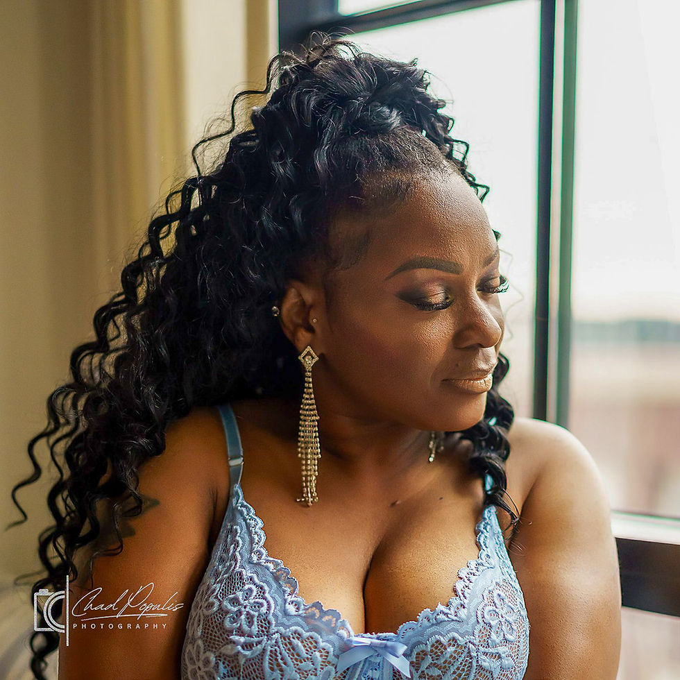 Woman in blue lace lingerie by a window, looking down thoughtfully; curly hair, gold earrings, Chad Womis Photography watermark