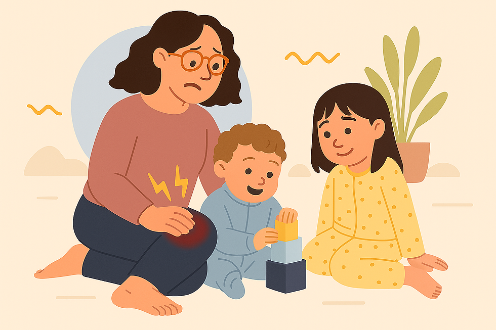 A thin white woman with shoulder-length brown curly hair sits indoors on a light tan background with soft abstract shapes. She wears casual clothing and glasses, with her hair styled naturally. She is playing with her light-skinned baby boy, who has curly light brown hair, and her light-skinned daughter, who has straight dark brown hair. Both children are in pyjamas. The practitioner’s posture shows visible discomfort in her knee, which is subtly emphasized.