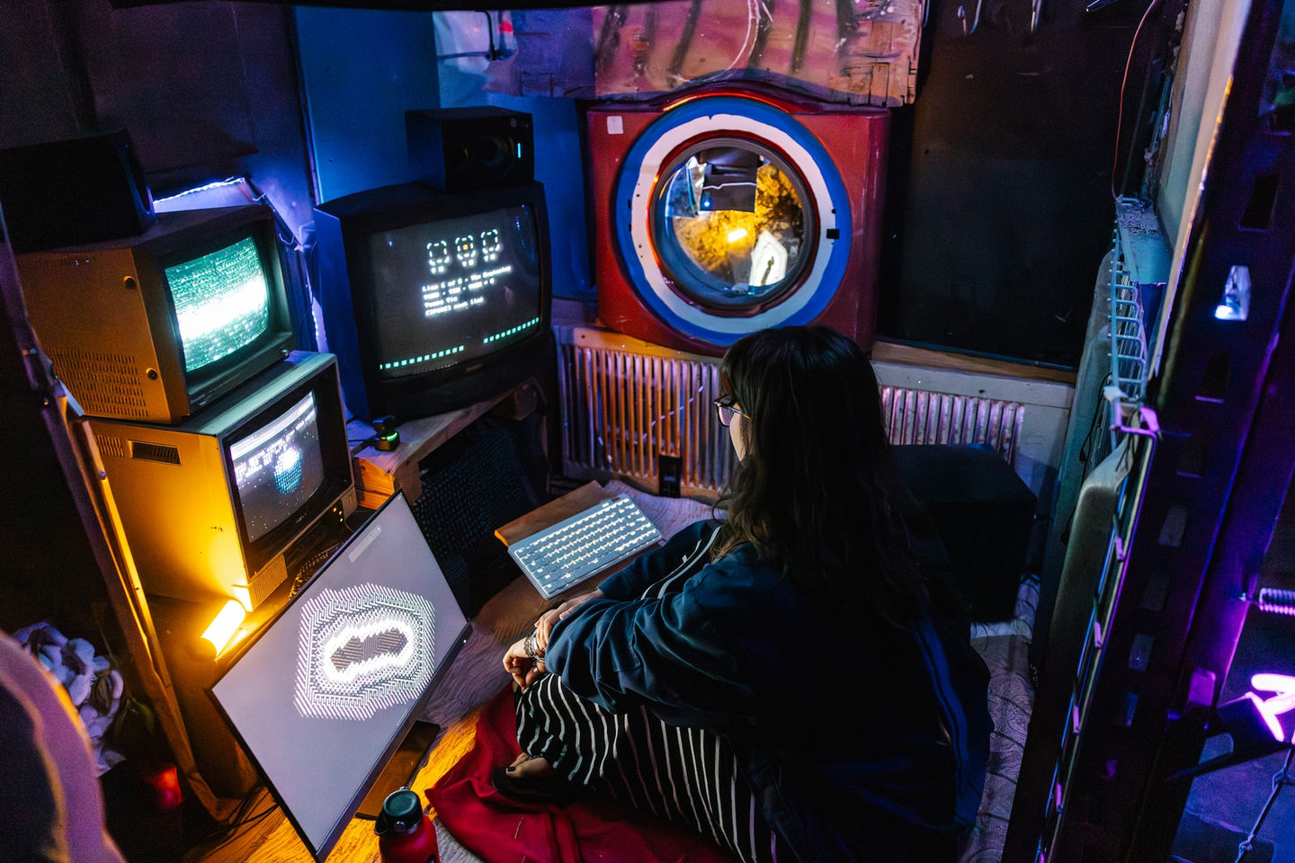 A visitor inside the Oracle Booth receiving a personalized generative reading, projections and CRT displays glowing in a dark room."