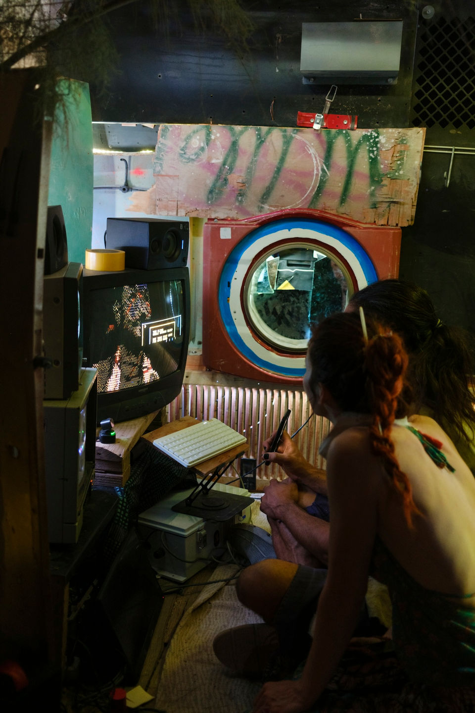 A visitor inside the Oracle Booth receiving a personalized generative reading, projections and CRT displays glowing in a dark room."