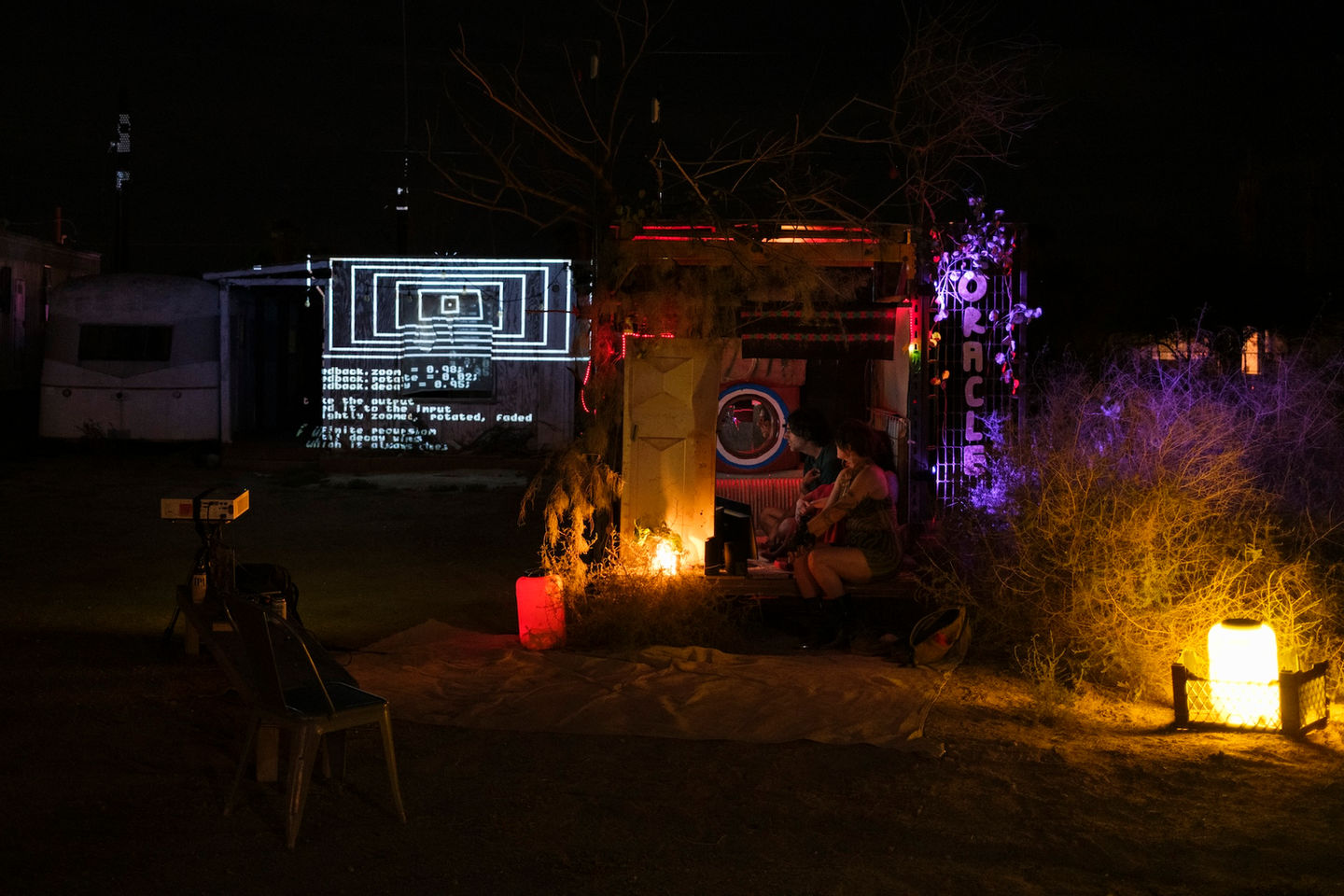 A visitor inside the Oracle Booth receiving a personalized generative reading, projections and CRT displays glowing in a dark room."