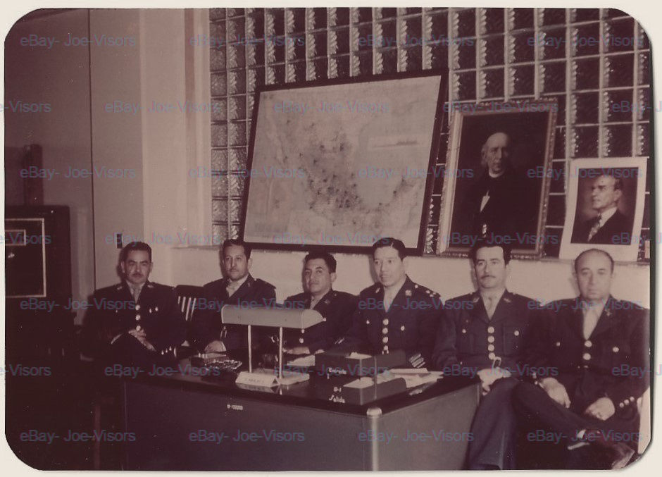 Five uniformed men seated at a desk, map and portrait on wall
