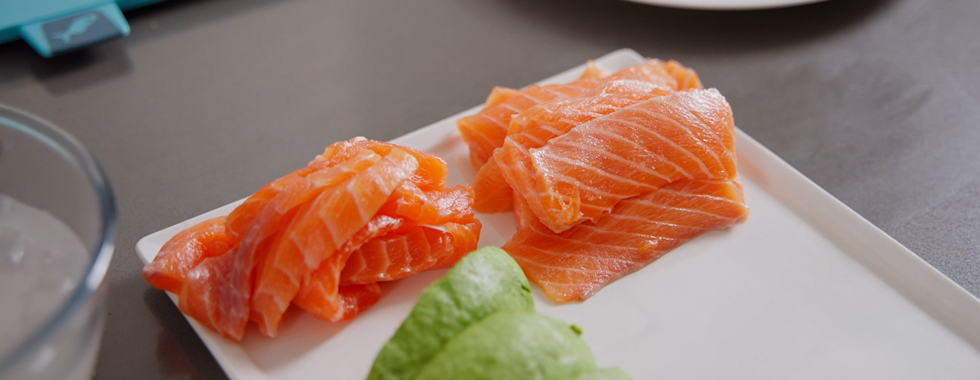 Fresh salmon slices, avocado, and cucumber strips arranged on a cutting board.