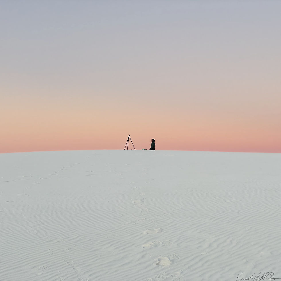 Woman and tripod rest on top of white dune with pink skies behind at White Sands National Park