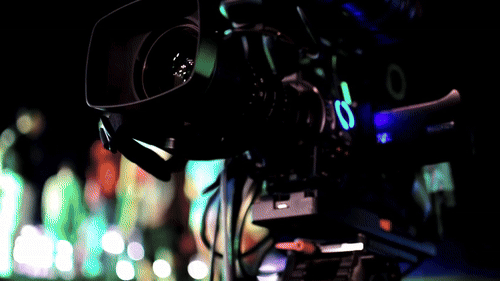 Close-up of a video camera filming a colorful, blurred stage with people in the background. Vibrant lights create an energetic mood of a Mitzvah party in Atlanta.