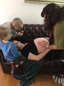 Midwife palpating pregnant belly with siblings looking on