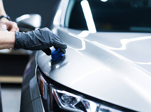 A gloved hand applying polish or coating to a car’s hood.