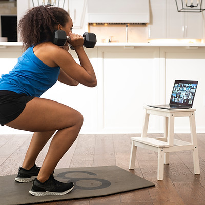 Woman does dumbbell squats, online workout, watching laptop screen Camp Gladiator.