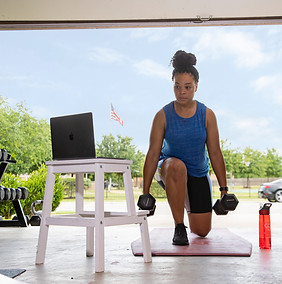 Woman does lunges with dumbbells during workout in home garage setup.