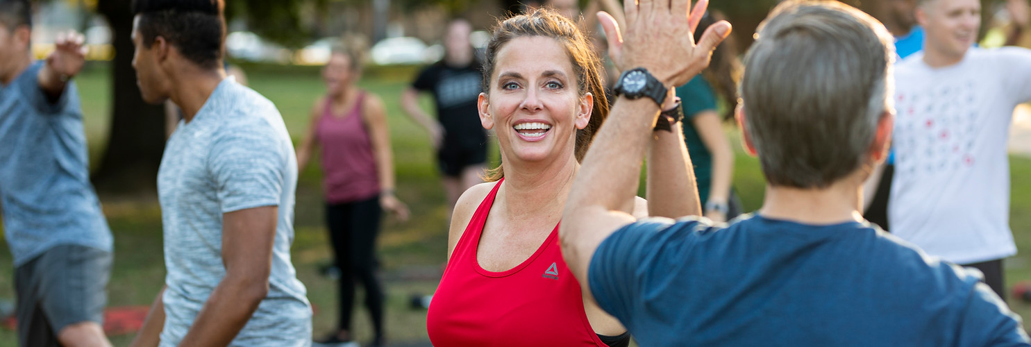 Woman giving high five, smiling during outdoor fitness class workout Camp Gladiator