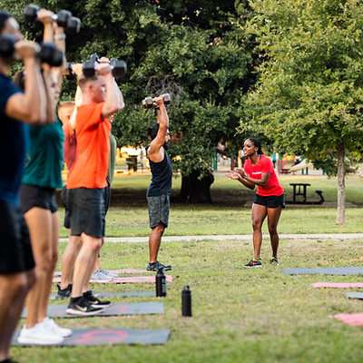 Group of people lifting weights during a workout session outdoors in the park.