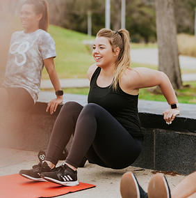Woman does tricep dips during Camp Gladiator workout session outdoors with two others.
