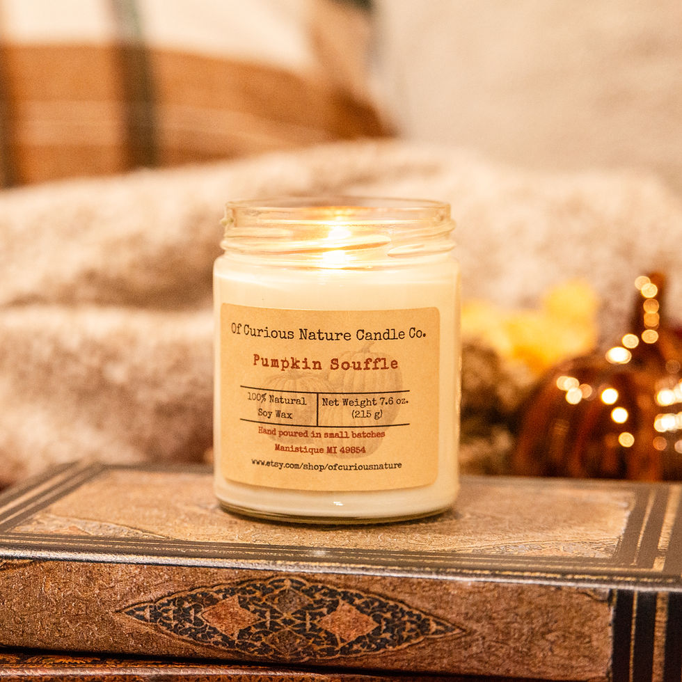 Pumpkin Souffle soy candle glowing in a clear glass jar on a vintage book with warm, cozy autumn decor.