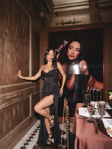 Posing beside a towering framed portrait of Shakira Khan, a guest in a black gown is documented by London events photographer Margot Jakobson at Carbone London.