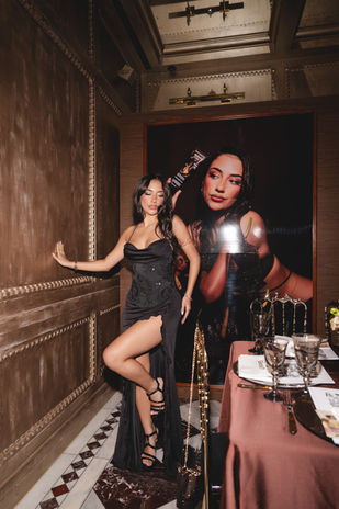 Posing beside a towering framed portrait of Shakira Khan, a guest in a black gown is documented by London events photographer Margot Jakobson at Carbone London.