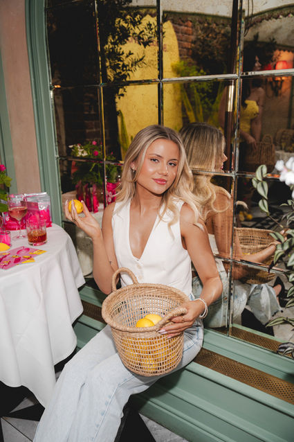 A woman in a white top holds a basket of lemons at Daphne's, with Beautyblender x Space NK products displayed on a nearby table. Photo by London event photographer Margot Jakobson.