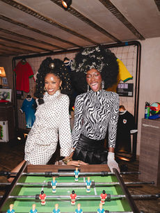 Two guests laugh over the Amazon Influencers foosball table amid hanging football shirts, an energetic frame from London events photographer Margot Jakobson.