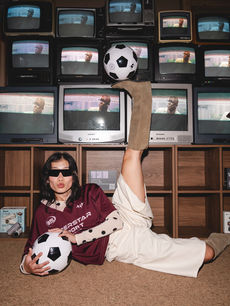 Reclined on the floor with one booted leg balancing a football against the retro TV wall, a guest is shot by London events photographer Margot Jakobson.