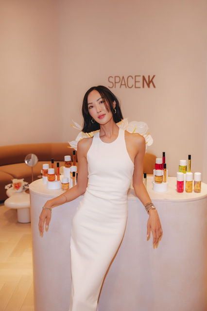 Captured by London event photographer Margot Jakobson, this image features a woman in a white dress holding Phlur fragrance at Space NK. The reflection in the mirror and floral decor highlight the elegance of the promotional event.