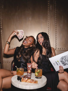 Waving playful banknotes over their cocktails, two guests laugh together in an image by London events photographer Margot Jakobson at the Garnier Olia launch.