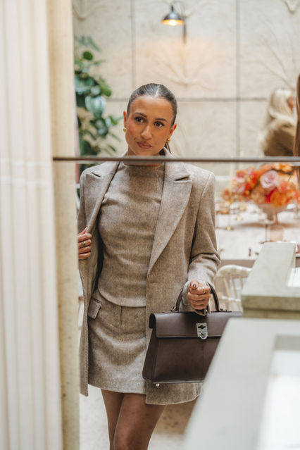 Event attendee in a chic grey ensemble with a brown leather handbag, photographed by event photographer Margot Jakobson at the 'Tandae' brand launch in London. 