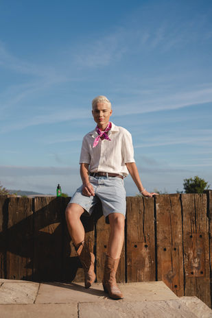 An influencer sits against the bright blue sky at Louma Retreat for the Matrix Hair staycation, styled in denim shorts and boots, photographed by London event photographer Margot Jakobson.