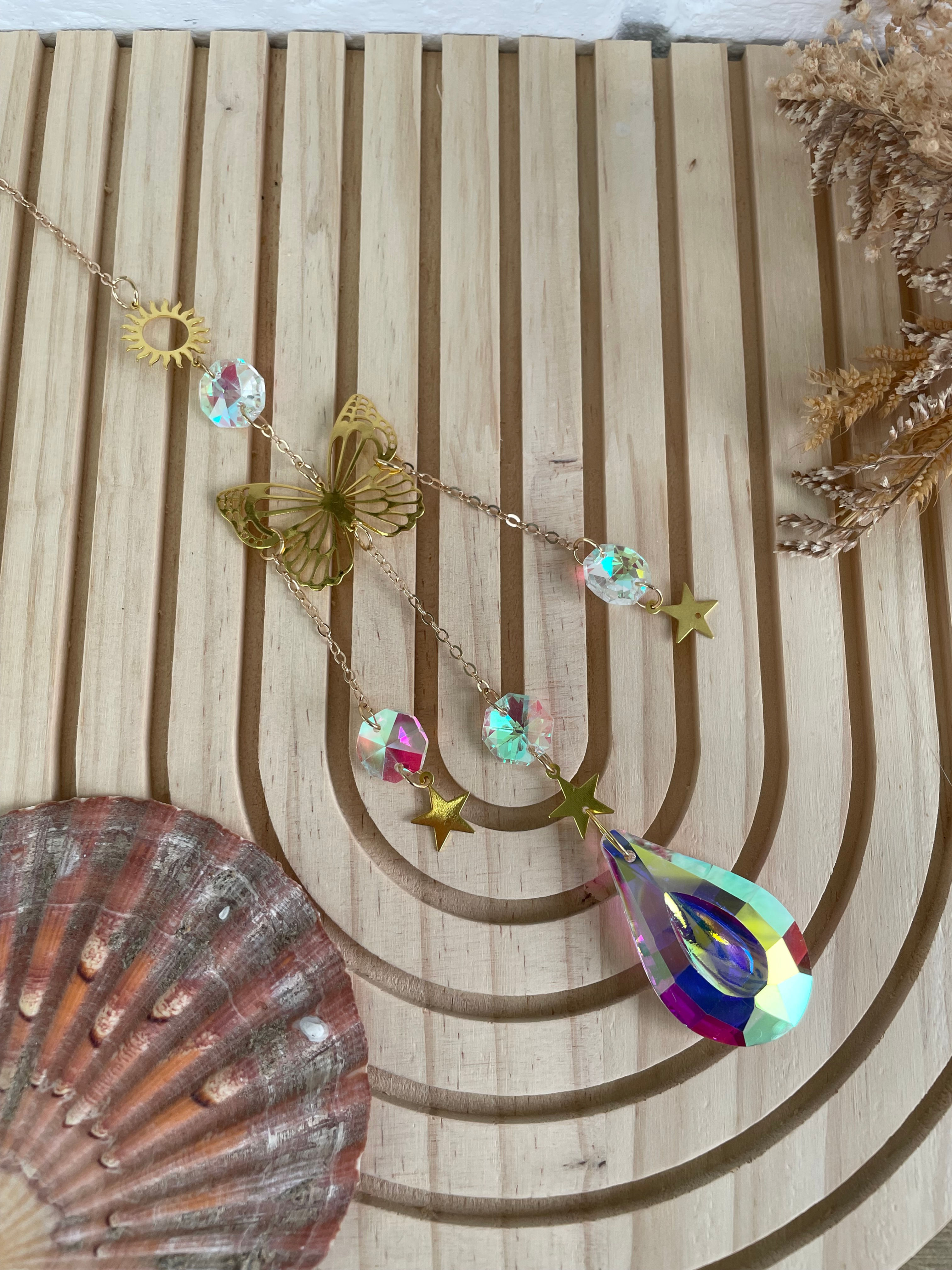 Collier fantaisie doré avec cristaux colorés et décorations sur fond bois clair.