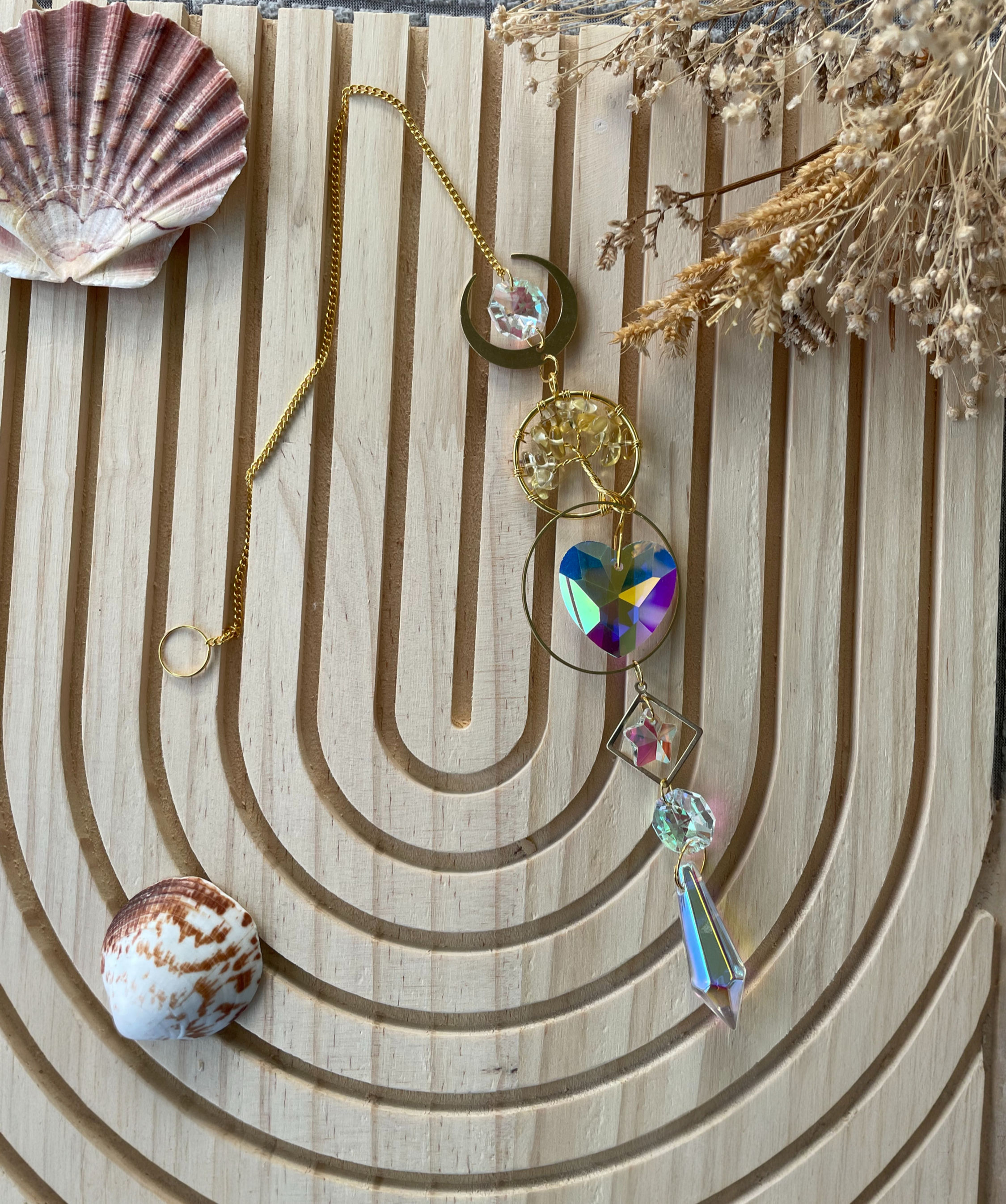 Bijoux dorés avec pendentifs et cristaux colorés, sur fond en bois clair.