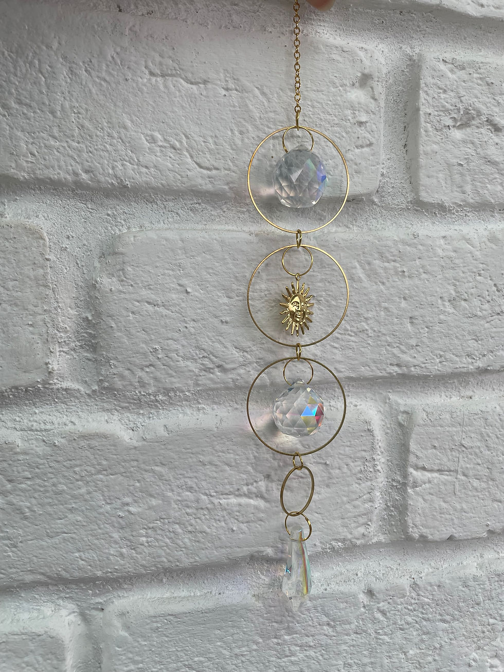 Miniature : Ornement suspendu avec cristaux et cercles dorés, sur fond de briques blanches.