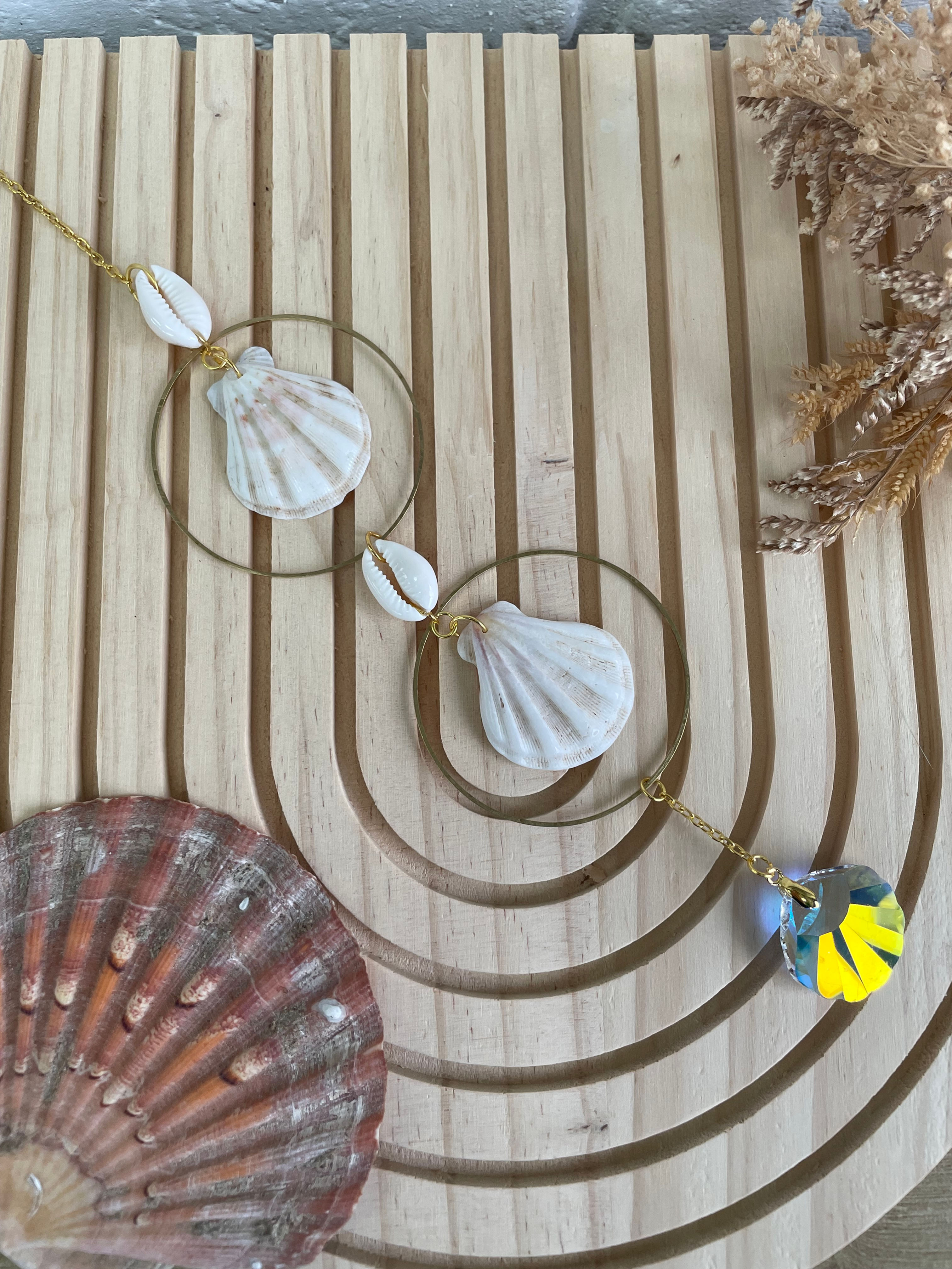 Colliers ornés de coquillages et cercles dorés, sur fond en bois clair.