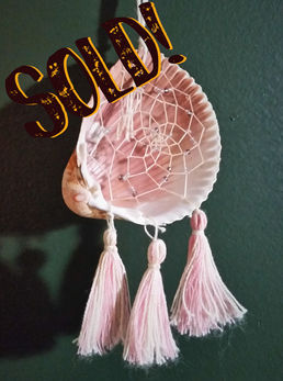 (Sold) A quahog shell dreamcatcher with a pink interior. Dreamcatcher web thread is decorated with clear and pink beads. There are three tassels on the bottom of the shell made of pink and white thread.