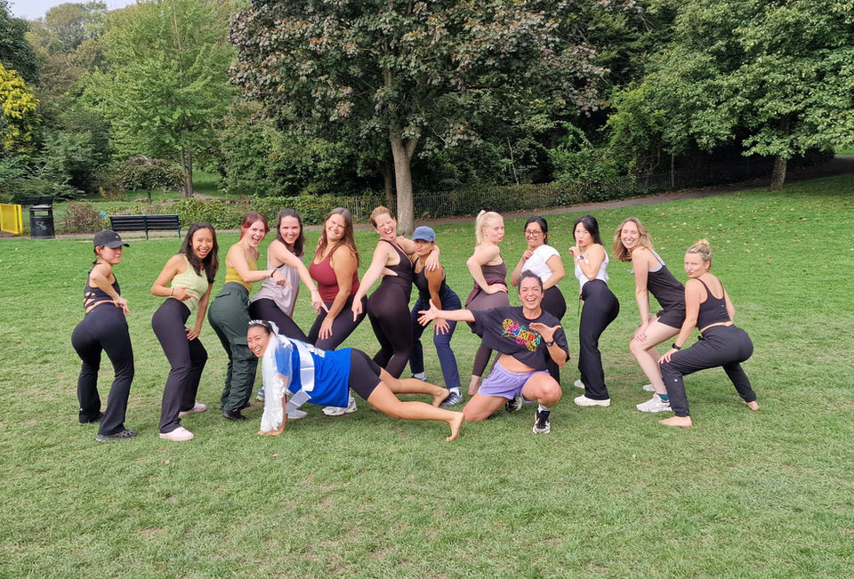 Group of woman posing for a group photo in a park.wearing leisure wear . Bride to be in the centre with the zumba instructor and her friends behind and around her. smiling an happy. Hen Do Zumba fitness class photo. trees and grass