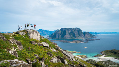 group of people jumping with a view of an island and fiords